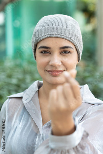 Happy smiling south asian Indian woman cancer patient wearing head scarf for hair loss after chemotherapy and radiation therapy showing heart hand gesture for cancer patient awareness