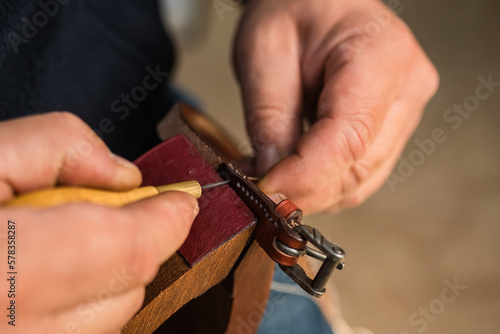 Man making holes in leather belt with stitching awl