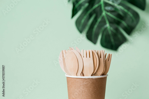 Eco-friendly disposable kitchen utensils in a paper cup on a beige-green background. Wooden forks, spoons and knives. Ecology, the concept of zero waste.