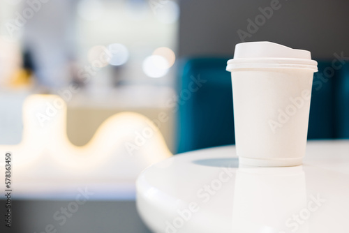 Takeaway white coffee cup on white table in the coffee shop  with empty space for design  text  or banner