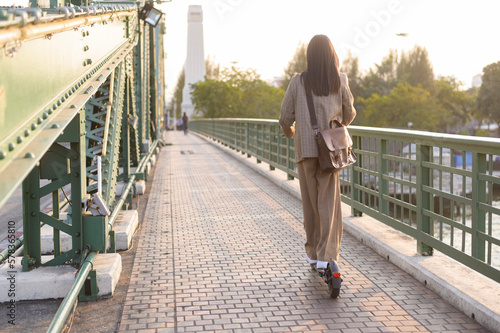 Portrait of young business woman with an electric scooter to work over bridge in modern city background