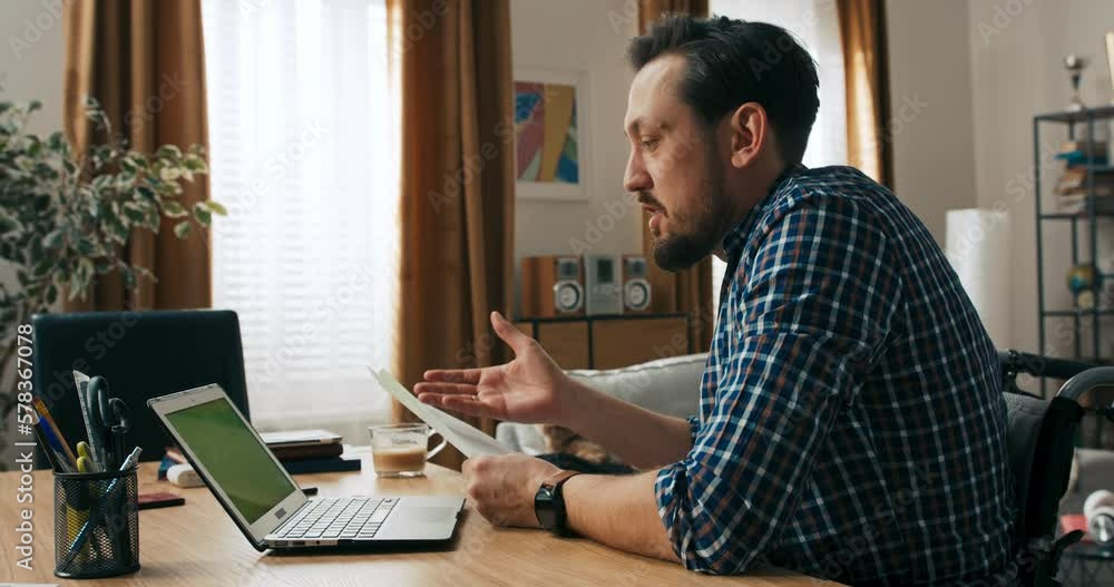Serious young siccessful beard man with dark hair sitting in wheelchair person with disabilities taking with employers having job interview conference online Serious young siccessful beard man with dark hair sitting in wheelchair person with disabilities taking with employers having job interview conference online