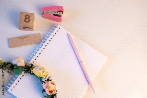 Material de oficina rosa con una corona de flores descansando sobre un cuaderno sobre un fondo rosa para el Día Internacional de la Mujer.