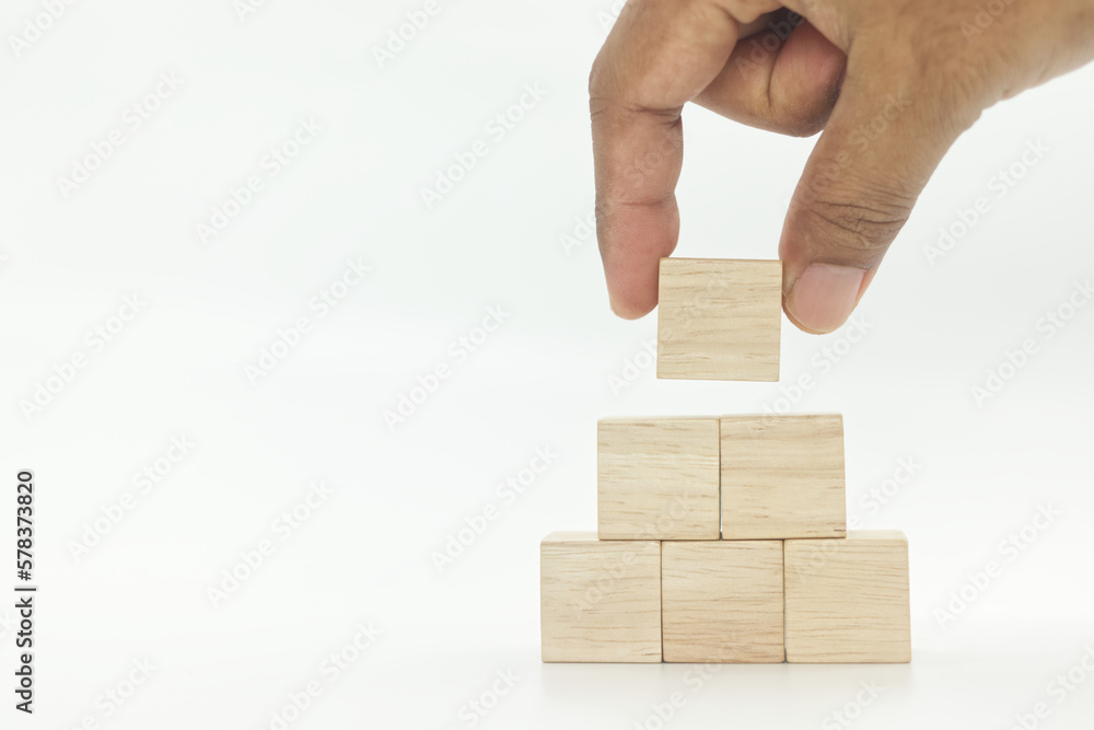 hand picking up wooden blank block cubes arranged in pyramid shape on white background hand picking up wooden blank block cubes arranged in pyramid shape on white background
