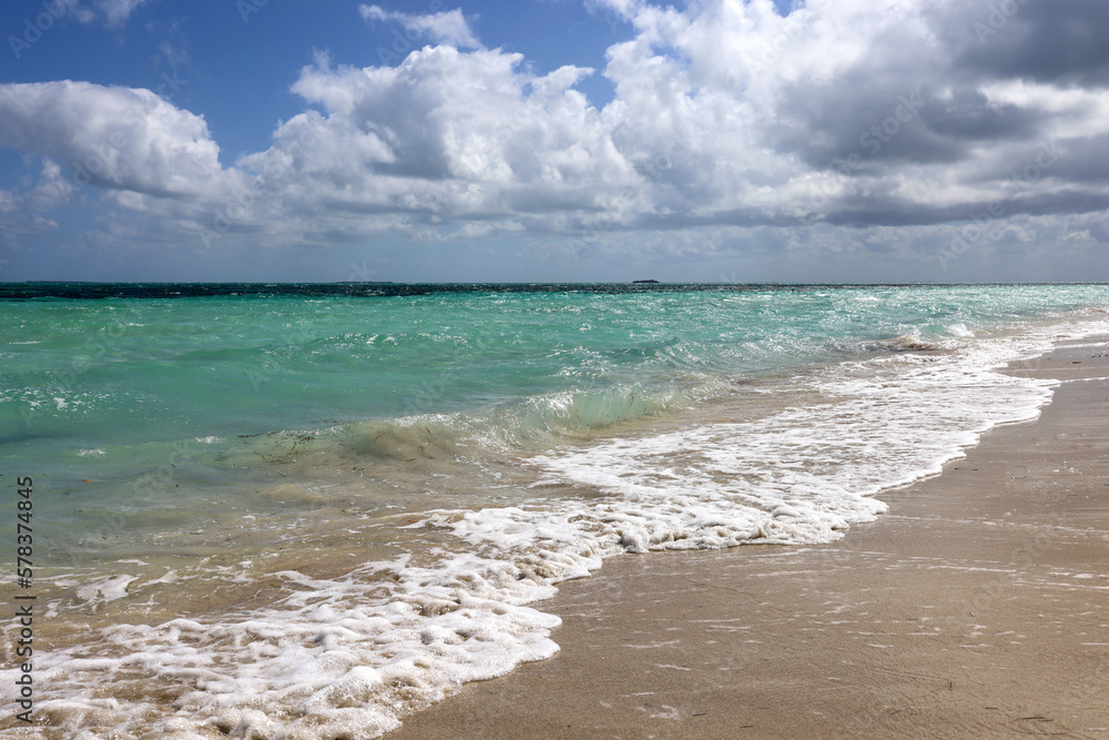 Waves breaking on a sand, view to ocean beach and sky with white clouds. Background for holidays on a paradise nature