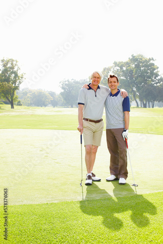 Two men on the golf course. Full length of father and son standing on golf course with arms around - copyspace.