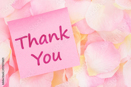 Thank you message on a pink sticky note with pink and yellow rose petals