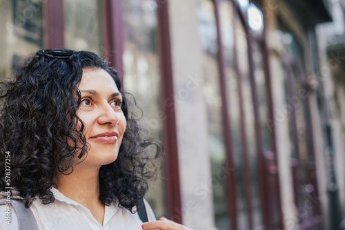 Close up portrait of a young woman with curly hair smiling. Windows of an old European street 