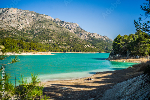 Lake Guadalest, rocky mountains and hills covered with trees. Blue sky