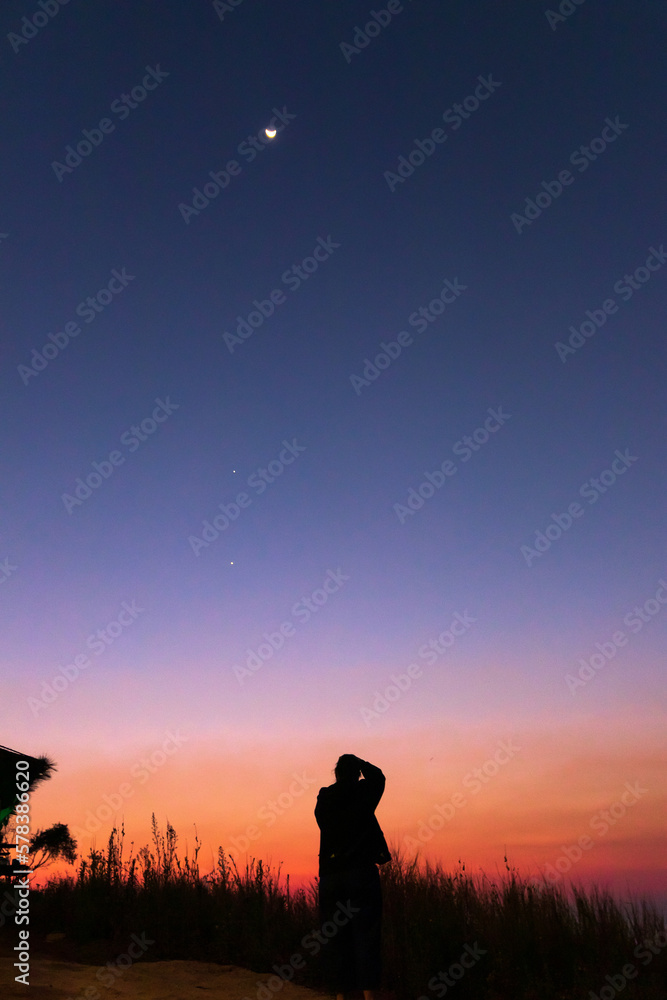 Women taking picture of nature observing evening sky with stars, planets and crescent moon. Moon meets Jupiter and Venus in the twilight sky.