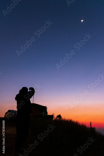 Women taking picture of nature observing evening sky with stars, planets and crescent moon. Moon meets Jupiter and Venus in the twilight sky.