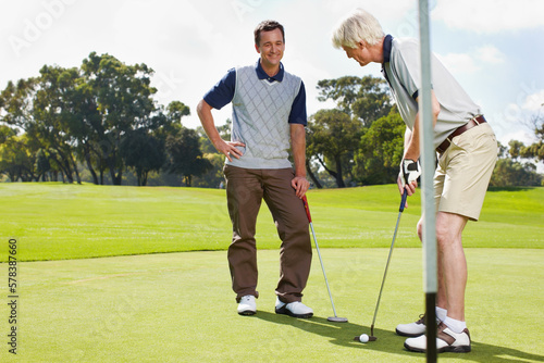 Golfing is a great way to bond. Two men out on the green playing a round of golf together.