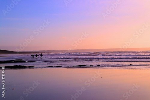 Silhouette of three surfers with surfboards walking into sea and waves and sunset