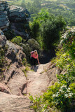 young woman hiking in the woods with backpack climbing rock