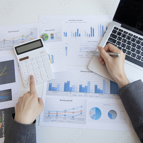Financial or accounting professionals use a laptop to analyze the company's revenue-expenses graph to prepare for presentation to the chief executive and partner, businesswomen working in the room.