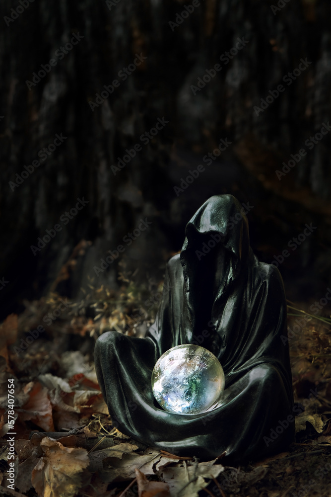 Magician mysterious black cloaked figure, Grim Reaper, with crystal ball in dark forest, blurred natural background. esoteric spiritual ritual for Samhain sabbat, Halloween holiday. Wiccan witchcraft
