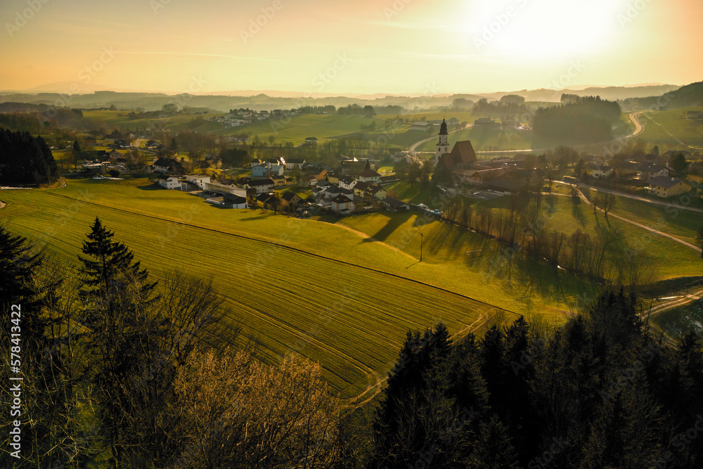 Fototapeta premium Wonderful aerial view of the evening atmosphere over Zell am Pettenfirst, Austria, where the old church and other buildings cast very long shadows