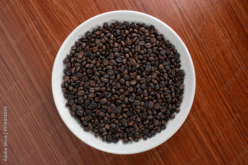 Coffee beans are placed on a plate with a wooden board in the background. There is space for text or something. Coffee beans are placed on a plate with a wooden board in the background. There is space for text or something.