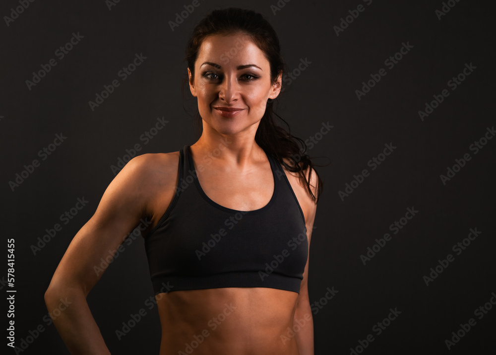 Confident sportswoman in sportsbra , holding hands on waist, fitness trainer standing in power pose, workout in gym isolated on black background Confident sportswoman in sportsbra , holding hands on waist, fitness trainer standing in power pose, workout in gym isolated on black background