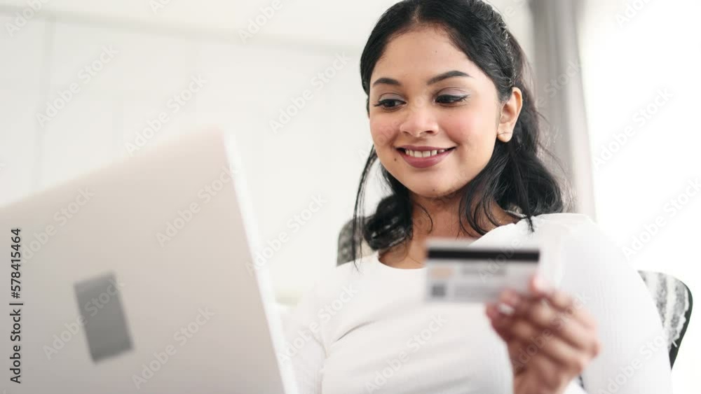 Portrait of young indian woman paying with credit card on laptop computer at home Happy customer doing payments online shopping in internet store and receiving cashback Easy pay concept Portrait of young indian woman paying with credit card on laptop computer at home Happy customer doing payments online shopping in internet store and receiving cashback Easy pay concept