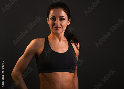 Confident sportswoman in sportsbra , holding hands on waist, fitness trainer standing in power pose, workout in gym isolated on black background © nastia1983