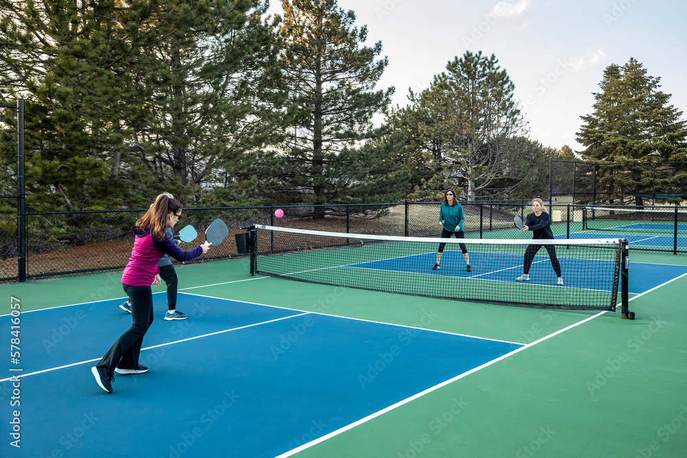 Obraz premium Four Female Pickleball Players Volley near the Net