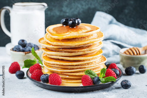 Delicious pancakes, with fresh blueberries, raspberry and maple syrup or honey on a dark background