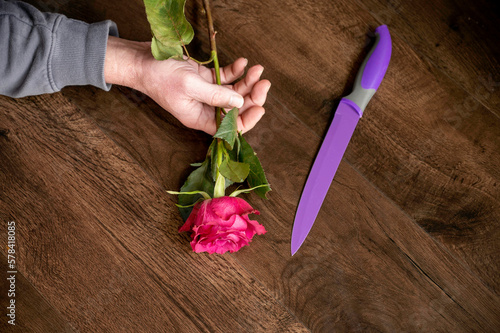 Hand holding rose on floor next to knife murder scene