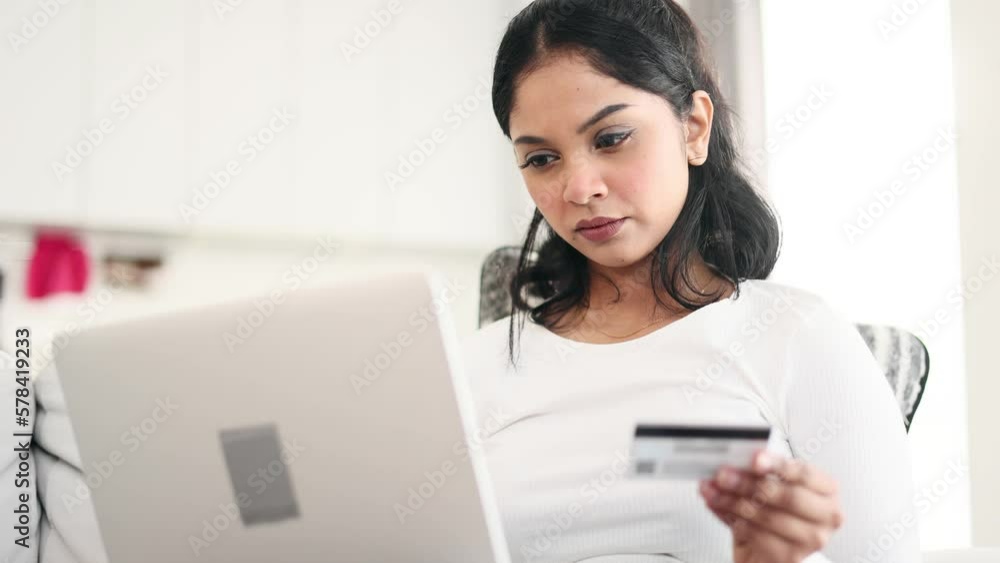 Portrait of young indian woman paying with credit card on laptop computer at home Happy customer doing payments online shopping in internet store and receiving cashback Easy pay concept Portrait of young indian woman paying with credit card on laptop computer at home Happy customer doing payments online shopping in internet store and receiving cashback Easy pay concept