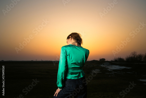 Fashion style portrait of young stunning woman posing in green silk blouse and denim trousers during sunset time  © triocean