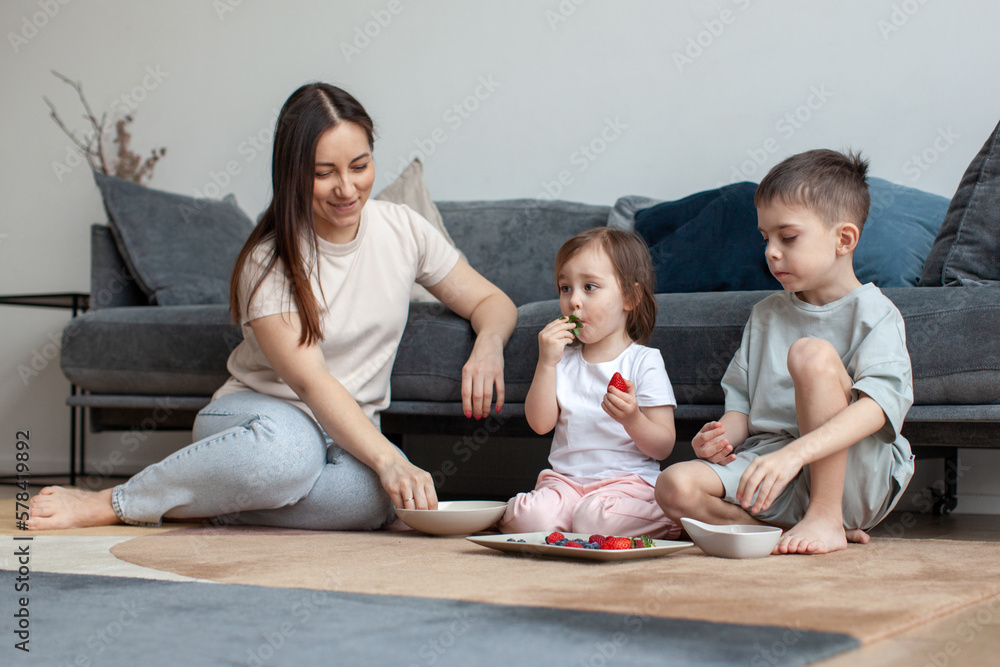 Mother and children eat berries. Breakfast on the floor. Modern interior. Mother and children eat berries. Breakfast on the floor. Modern interior.
