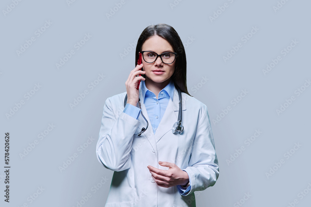 Young female doctor talking on mobile phone, on light gray background Young female doctor talking on mobile phone, on light gray background