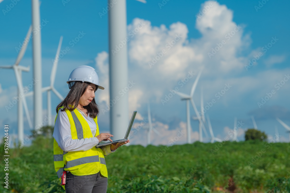 women engineer working and holding the report at wind turbine farm Power Generator Station on mountain,Thailand people