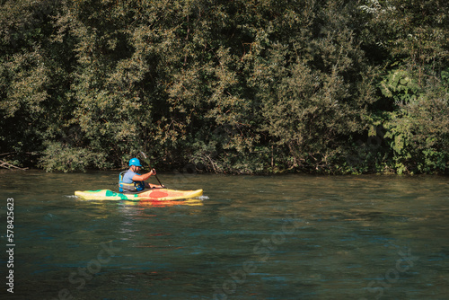 Caucasian man kayaking over the mountain river rapids, with the beautiful rocky bank and green forest in the background. Water sport