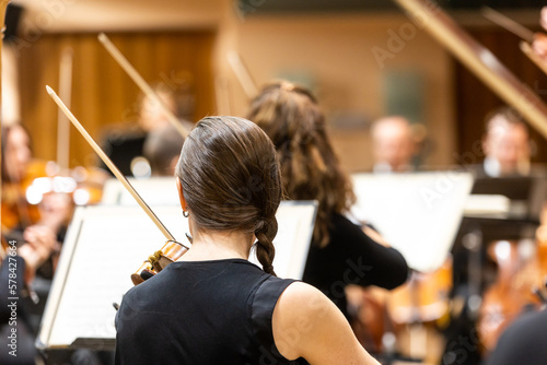 Professional symphonic string orchestra performing on stage and playing a classical music concert, violinist in a foreground