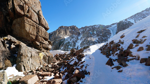 Snowy high mountains with bright sun and rocks. Moss grows in places on huge stones. Blue ice breaks through the snow. Glacier under the snow. A place where the soul and body of a climber rest.