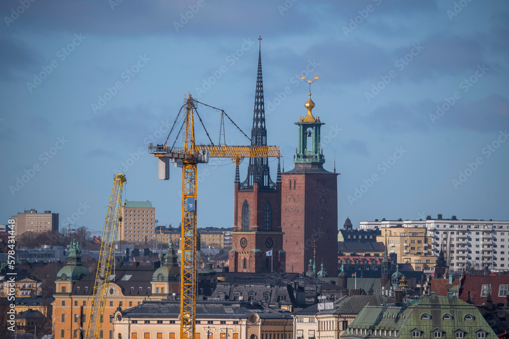 A crane, the tower of the church Riddarholms Kyrkan and the Town City Hall, roofs and facades in the old town Gamla Stan, a sunny spring day in Stockholm