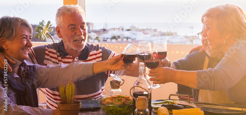 Mature men and women group celebrate and toasting with red wine all together enjoying lunch leisure activity having fun and smiling. Retired people eating and drinking in friendship. Outdoor table