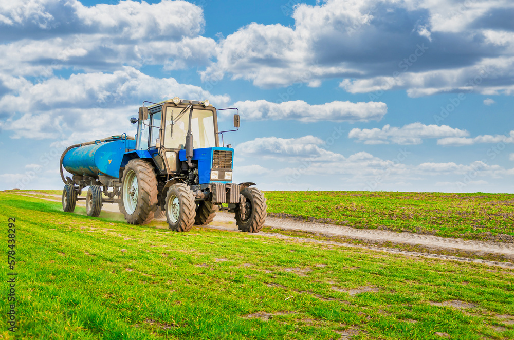 An agricultural tractor drives along a field road. Spring Field An agricultural tractor drives along a field road. Spring Field