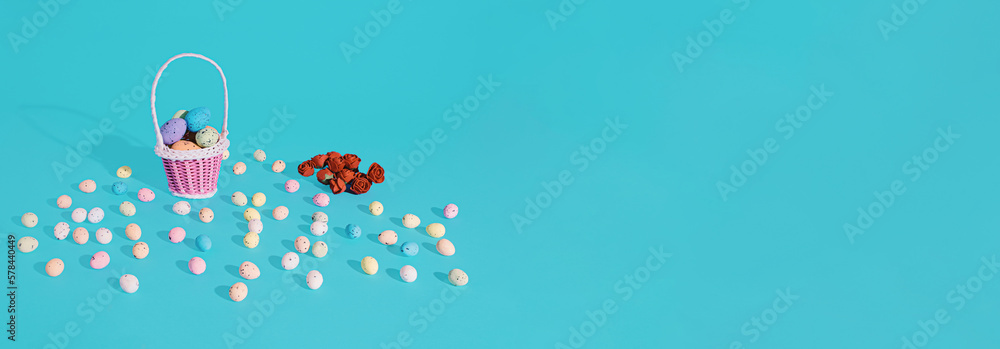 Easter eggs in basket and red roses on cyan background. Minimal horizontal composition, banner with copy space, spring and Easter decoration concept