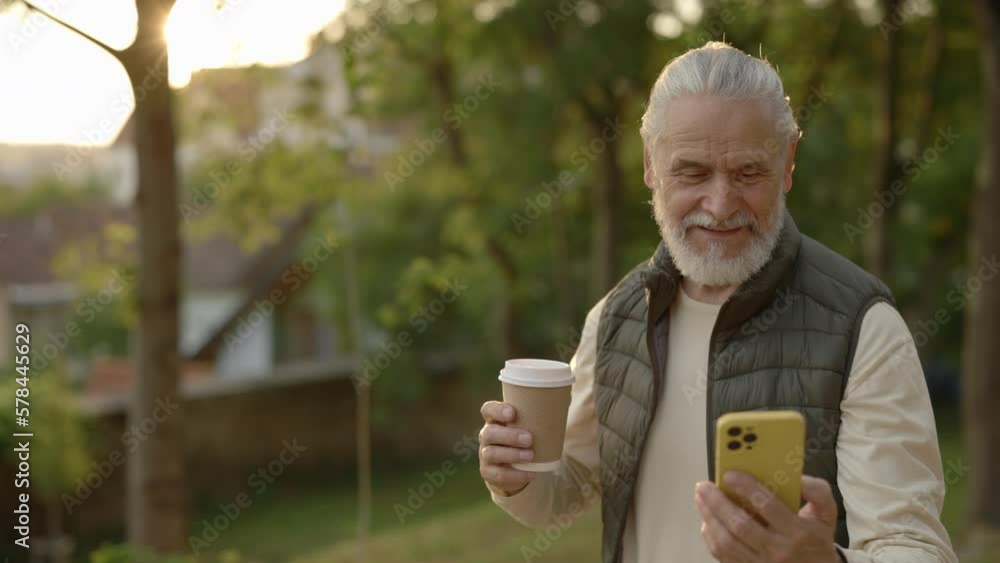 Cheerful Serion Man Using Smartphone and Carrying Cup of Coffee While Walking in the Park. Active Pensioner Outside. Eldery Male Enjoy Beautiful Life. Modern Lifestyles. Cheerful Serion Man Using Smartphone and Carrying Cup of Coffee While Walking in the Park. Active Pensioner Outside. Eldery Male Enjoy Beautiful Life. Modern Lifestyles.