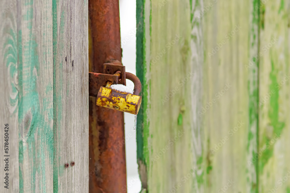 An old rusty padlock is covered with snow on a wooden fence