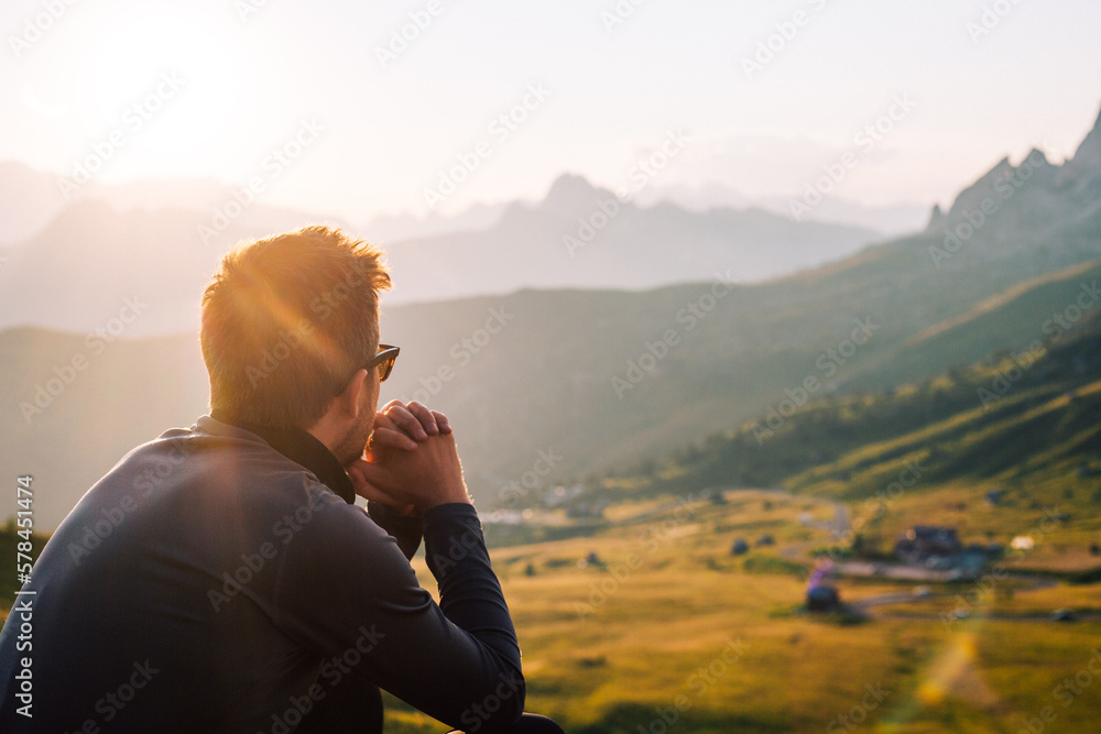 Person mit Sonnenbrille sitzt in den Bergen bei Sonnenuntergang und genießt die Natur  - obrazy, fototapety, plakaty 