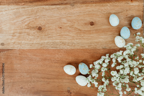 Dyed eggs and white small flowers lie on wooden brown table. Space for text. Mock up. Wooden background with blue and white eggs and white flowers for easter. 