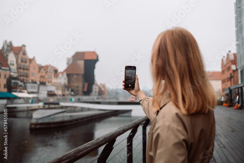 Outdoor summer smiling lifestyle portrait of pretty young woman having fun in the city in Europe in evening with camera travel photo of photographer. Gdansk, Poland