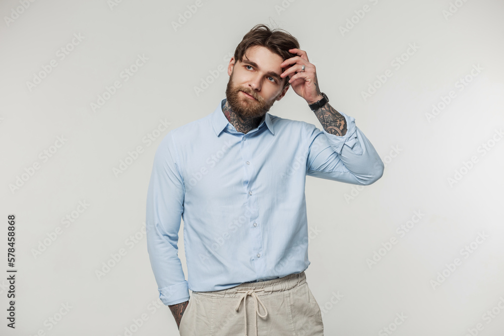 Stylish successful hipster business man with hair and beard with a tattoo in fashionable casual clothes with a shirt on a white background Stylish successful hipster business man with hair and beard with a tattoo in fashionable casual clothes with a shirt on a white background