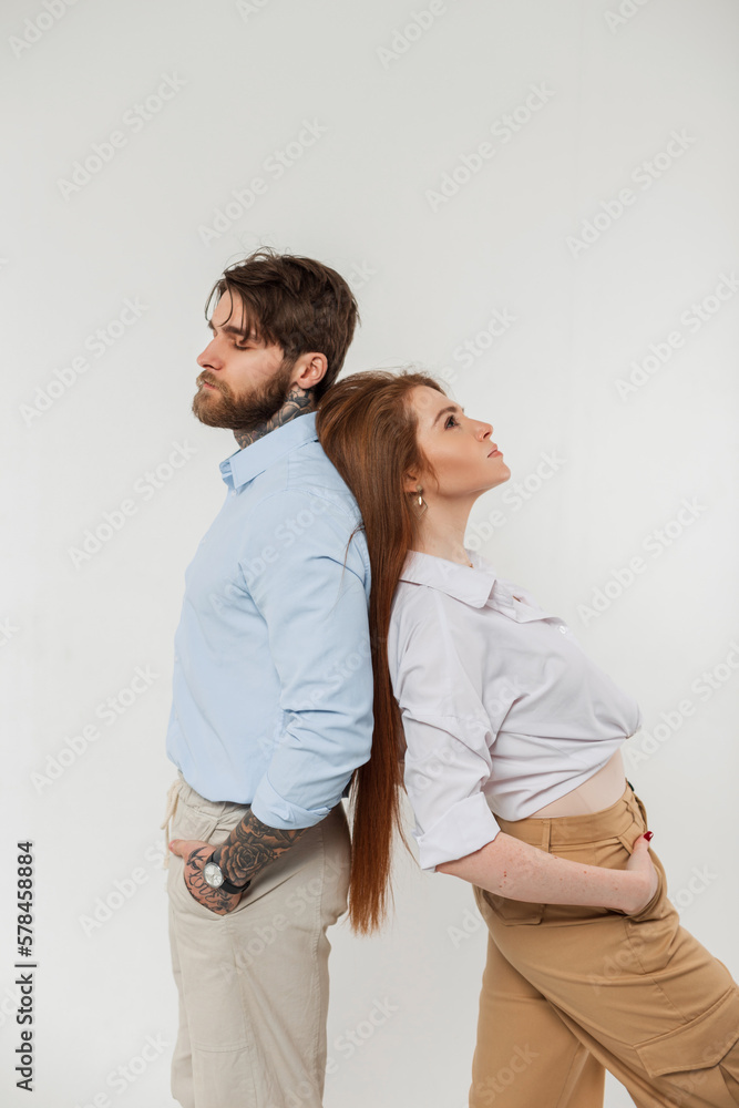 Fashionable handsome couple handsome hipster man and beautiful redheaded woman in stylish casual clothes with shirt standing back to back in the studio Fashionable handsome couple handsome hipster man and beautiful redheaded woman in stylish casual clothes with shirt standing back to back in the studio