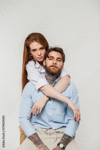 Fashionable young beautiful couple pretty woman and hipster handsome man in stylish casual outfit with shirt sits and hug on a white background