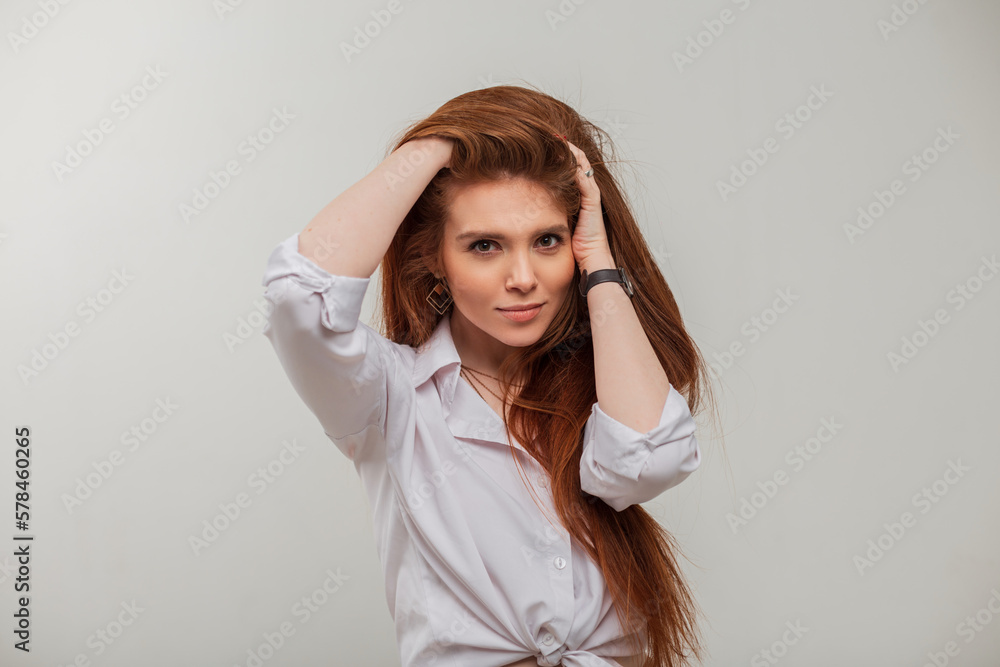 Fashionable beautiful redhead model girl with long red hair in stylish white elegant clothes poses on a grey background in the studio Fashionable beautiful redhead model girl with long red hair in stylish white elegant clothes poses on a grey background in the studio