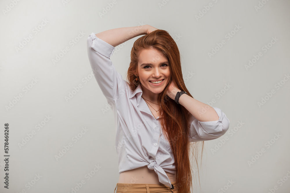Fototapeta premium Happy redhead fashion fresh girl with a cute smile in a white shirt poses on a white background in the studio
